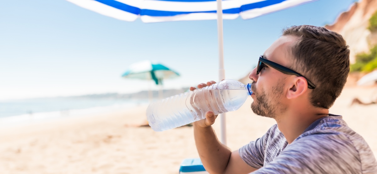 young man green solar umbrella drinks water beach